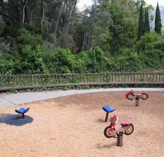 A neighborhood park with close-up views of the mountains. large lawn, playground, autumn trees, and bridge over creek to school.