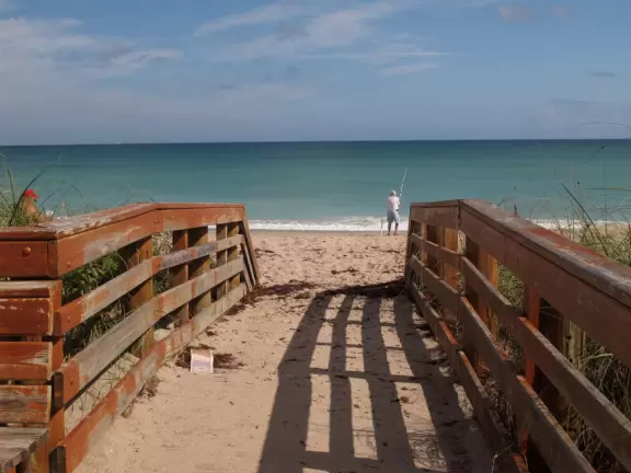 One of many beach access points leading to a shadeless beach with bright turquoise water.