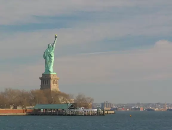 A boardwalk lined with classic lampposts and benches, with views of the bay and the statue of liberty!
