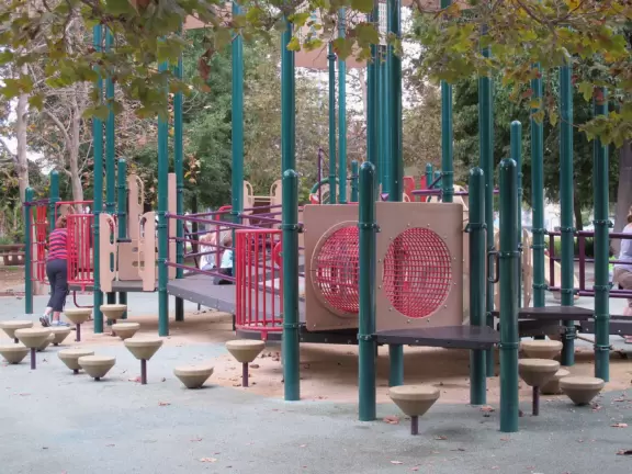 Plain-looking playground with lots of interesting climbing structures, tunnels, slides, stepping stones, bridges, swings, pretend construction trucks to drive, a giant shaded sand pit with sand funnels, all in a very urban landscape.