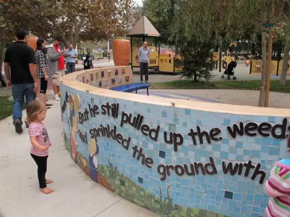 Plain-looking playground with lots of interesting climbing structures, tunnels, slides, stepping stones, bridges, swings, pretend construction trucks to drive, a giant shaded sand pit with sand funnels, all in a very urban landscape.