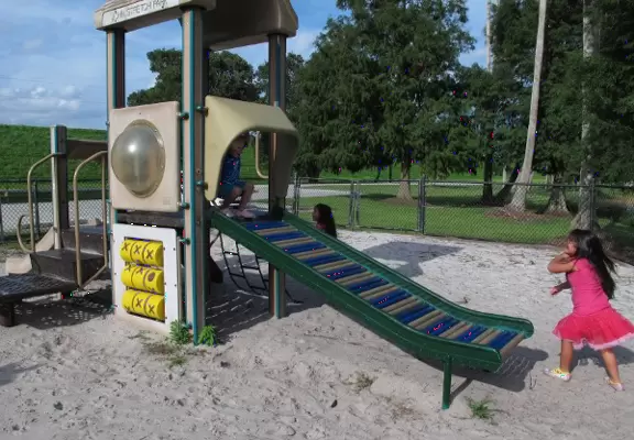 A small playground by a lake with palm trees, picnic pavilion, and some mechanical items to explore such as a diesel engine.
