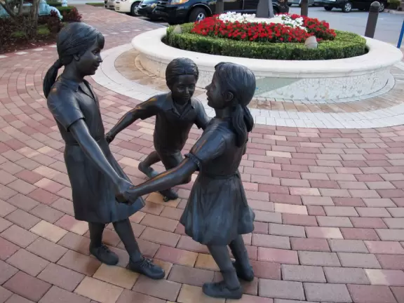 Small shopping plaza with attractive landscaping and design, and beautiful bar area with yellow chairs and tables, fountains, and flowers.