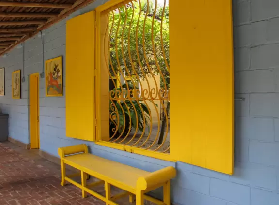 Colorful plantation-style house with courtyard full of tropical palms and orchids, lovely architecture, and lagoon with giant banyan tree.