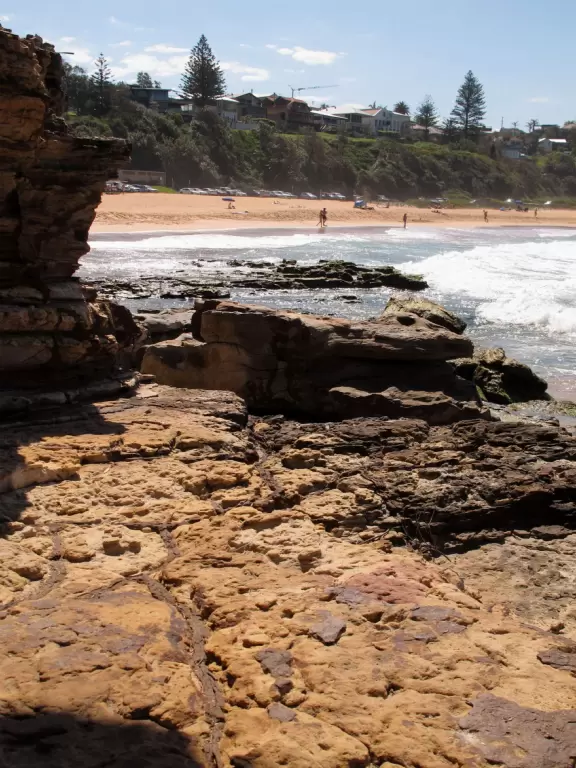 Stunning beach with orange-pink sand, blue-green water, gorgeous flower-studded headland, and rock pools that kids love to explore.
