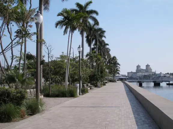 Wide walking path along the water with tropical flowers, piers, grand high rises, and palm trees- no shade though.