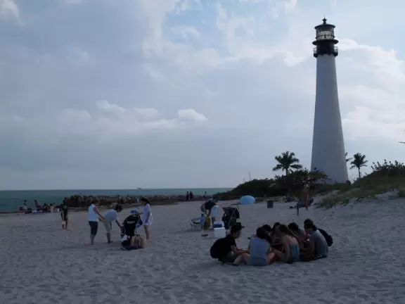 Picturesque beach with white lighthouse, happy people, and turquoise water.